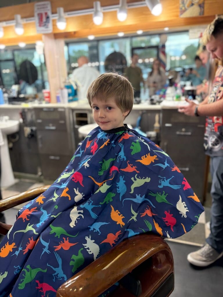 A young boy in a dinosaur cape before his haircut at The Cut Above of SRQ